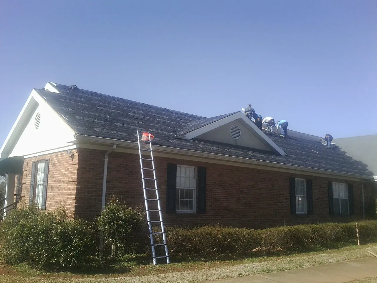 Crew tearing shingles off a brick ranch roof with a ladder set — Metal Roof Repair work by our crew in Madisonburg