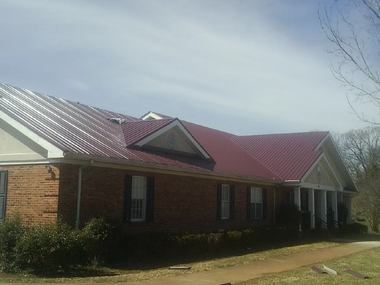 Red metal roof with gabled entries on a long brick building, from a Hail Damage Roof Repair job in Madisonburg