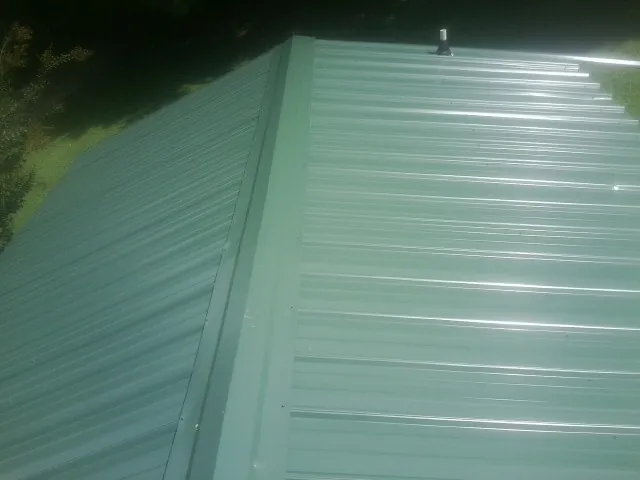 New green metal panels meeting at the ridge of a roof — Flat Roof Repair work by our crew in Madisonburg