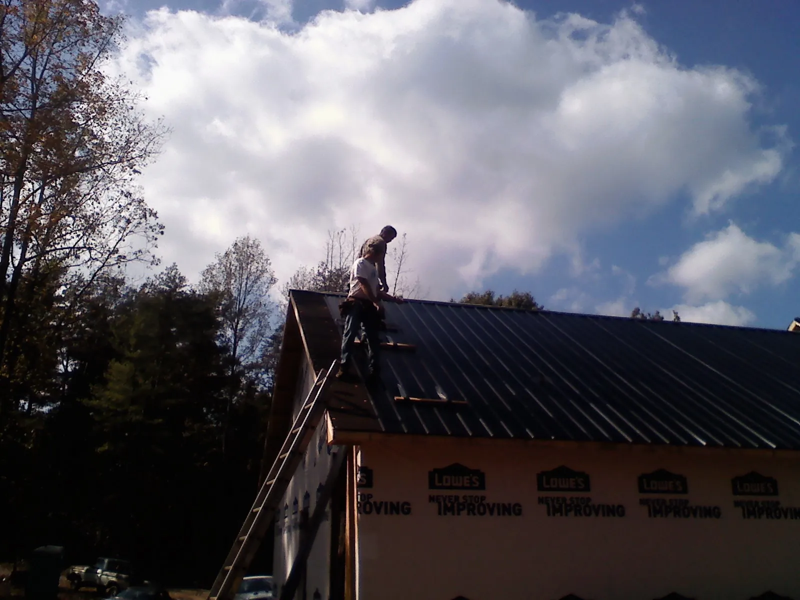 Roofer fastening dark metal panels high against a cloudy sky, from a Roof Inspection job in Madisonburg