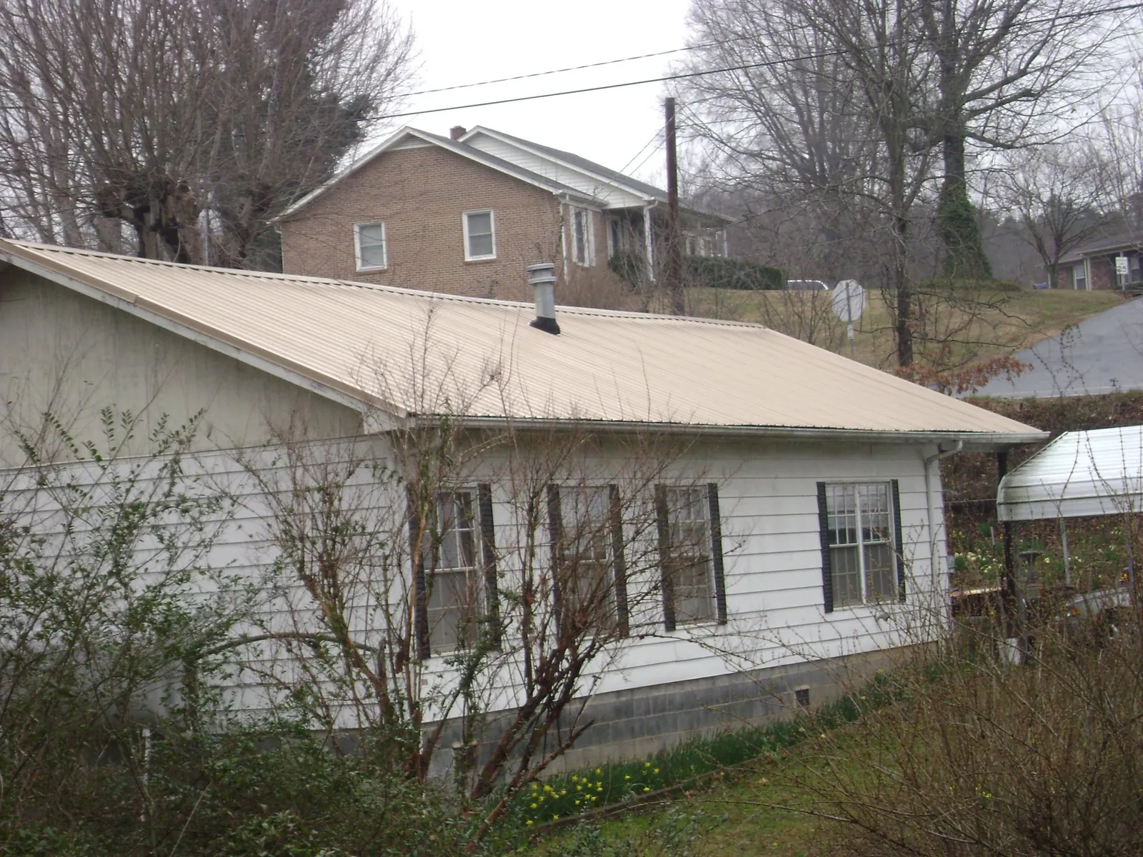 Tan metal roof on a white sided house set into a hillside — Commercial Roofing by Roofing Brothers in Madisonburg