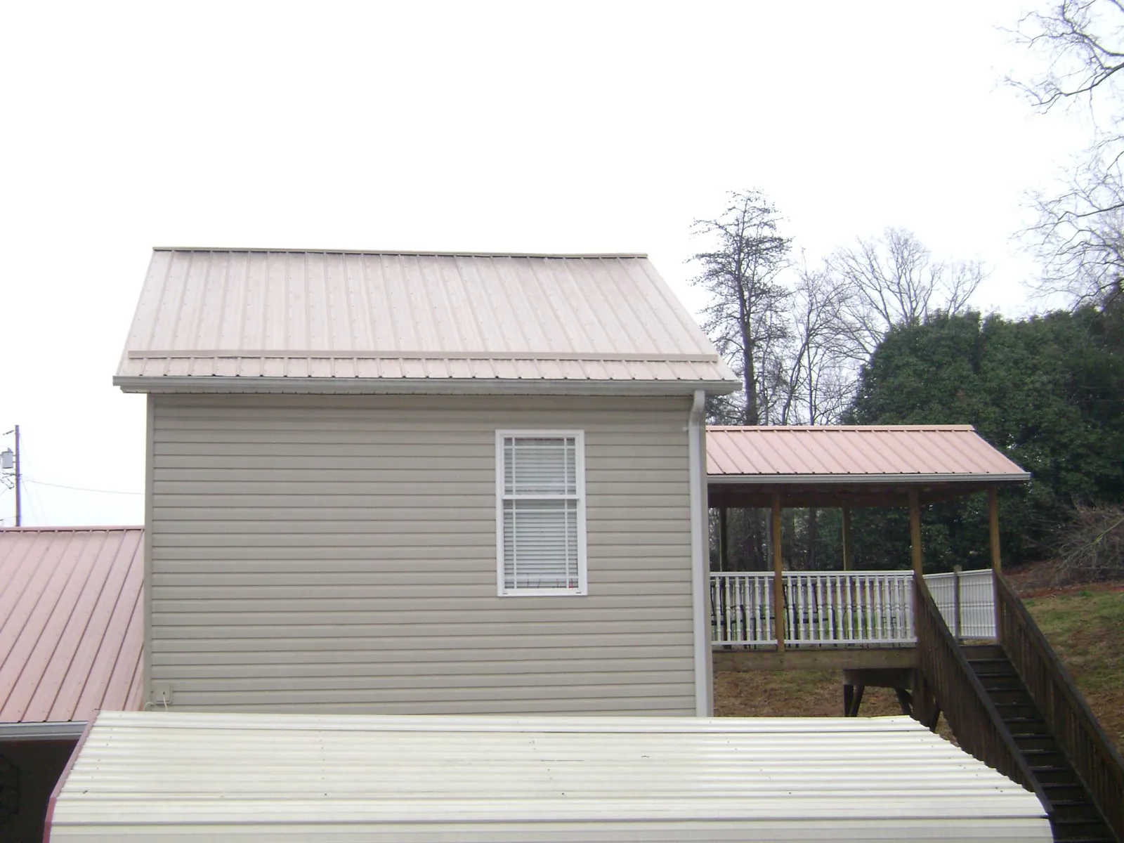 Tan metal roofs on a two story addition and attached porch, from a Roof Replacement job in Madisonburg